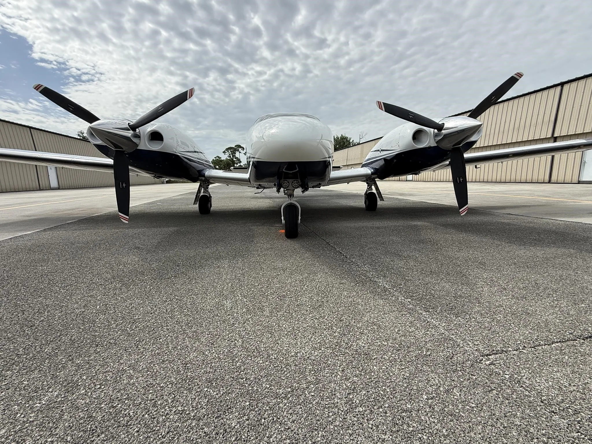 A head-on view of a white and blue Piper Seneca V aircraft parked on an airfield tarmac.