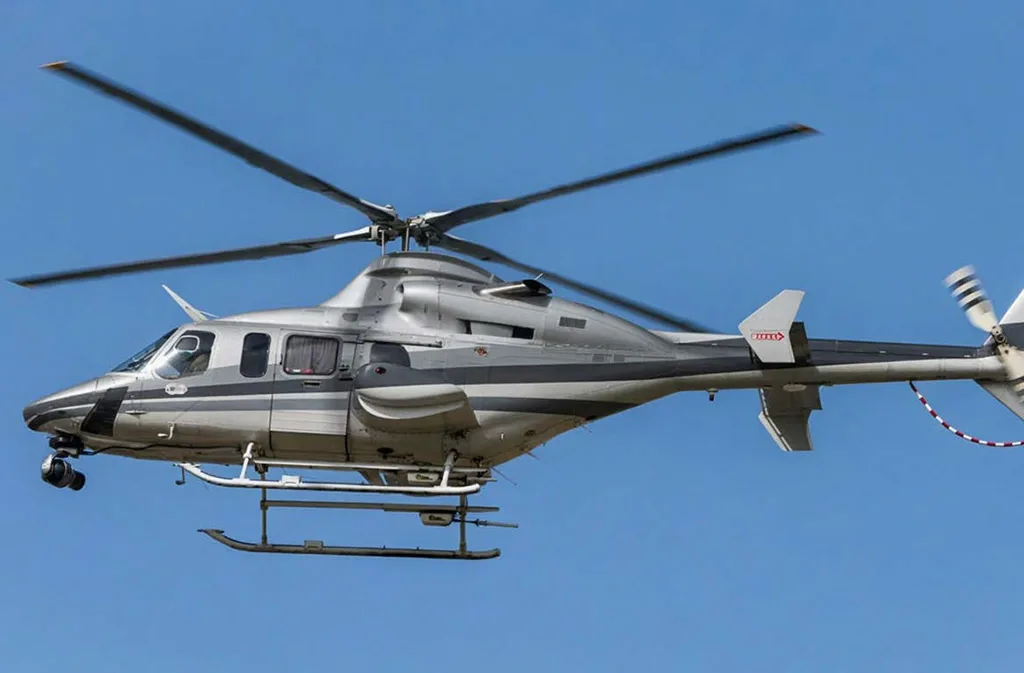 A silver helicopter with dark grey stripes flies against a clear blue sky.