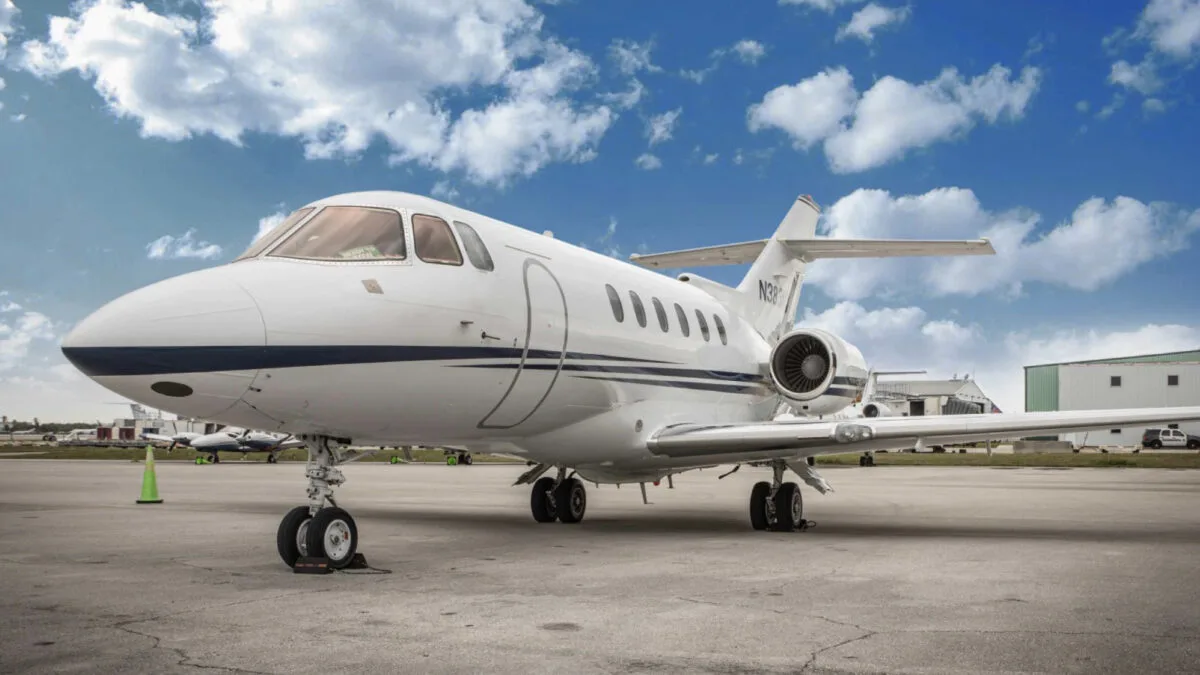 A white business jet with a blue stripe, registration N383MV, parked on an airport tarmac under a partly cloudy sky.