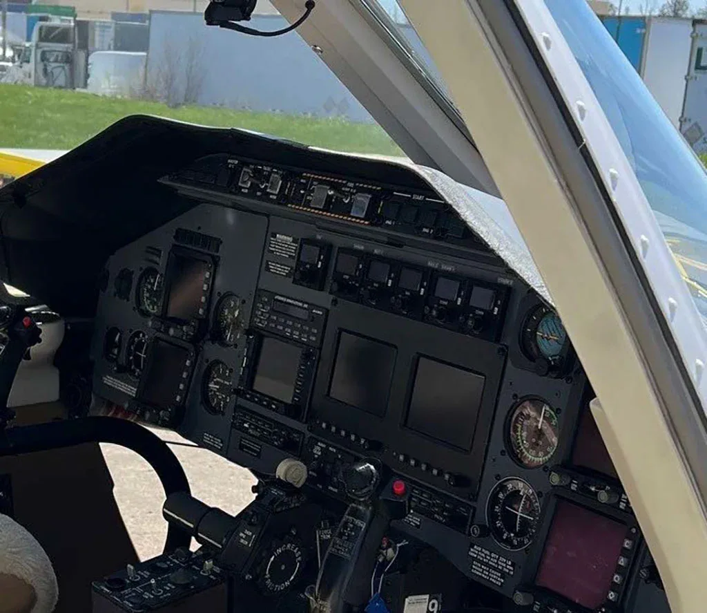A close-up view of a helicopter cockpit with multiple screens and analog gauges on the instrument panel.