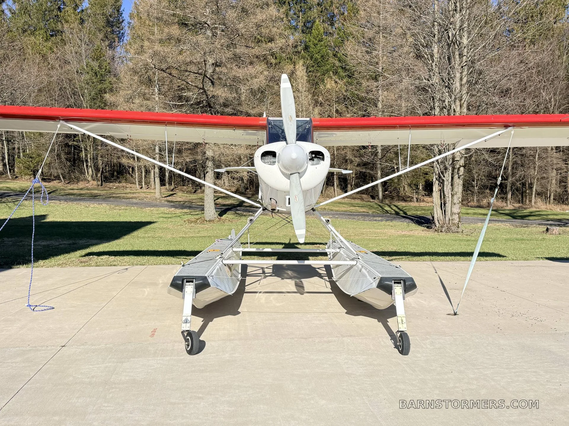 Front view of a white and red Aviat Husky A-1 floatplane (N817JV) parked on concrete.