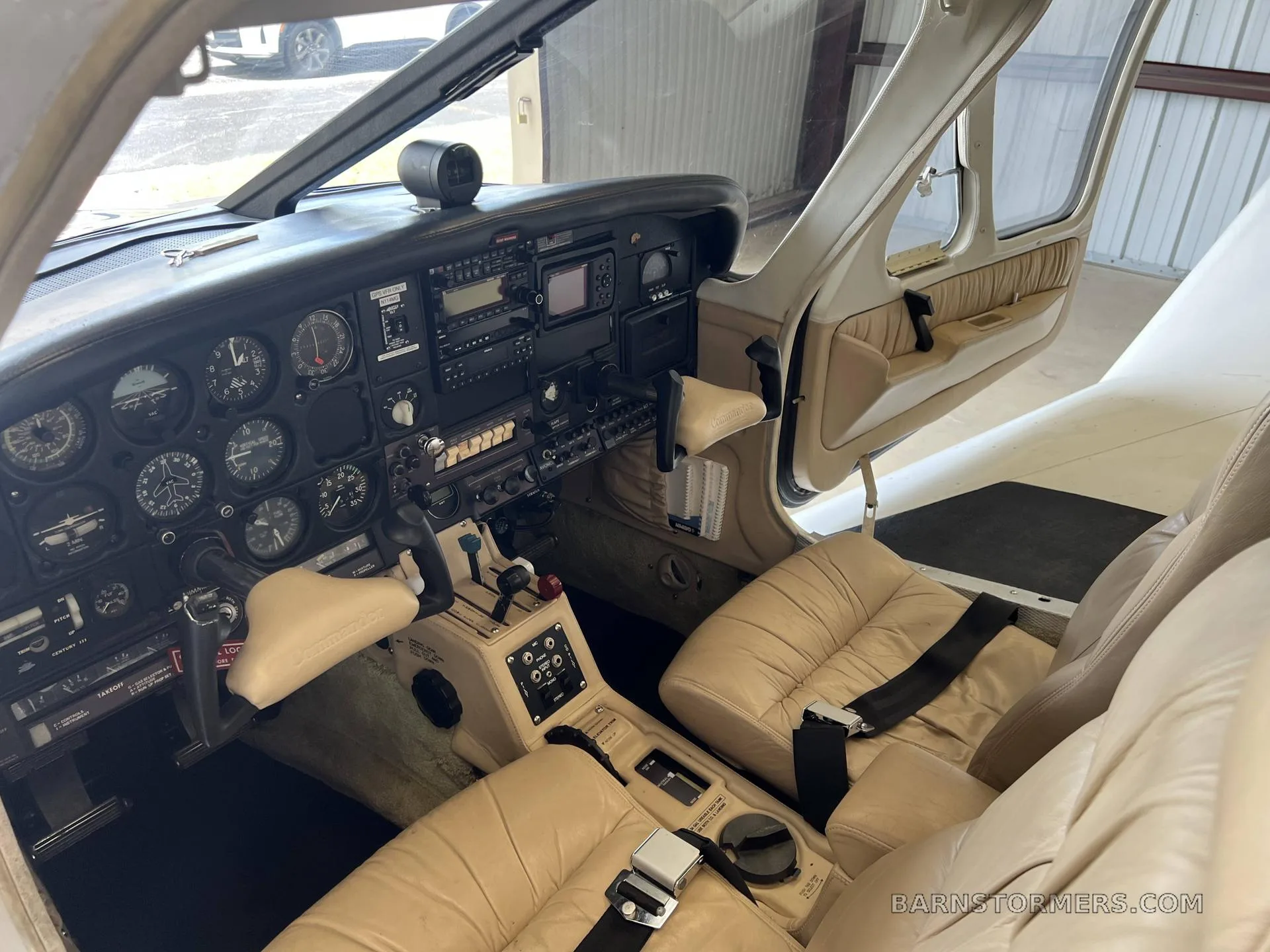 A view of the beige cockpit and front cabin of a Commander aircraft with the door open, showing the instrument panel and controls.