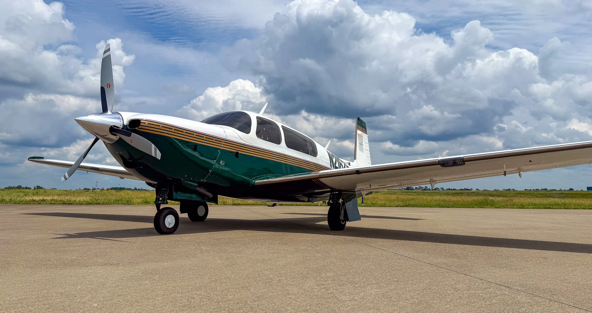 A white and green Mooney M20 aircraft with registration N21625 parked on an airfield under a cloudy sky.