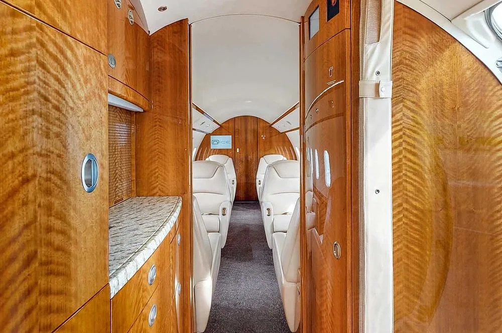 The aircraft cabin interior showing a galley area with wood cabinetry and a granite countertop, looking towards the passenger seating.