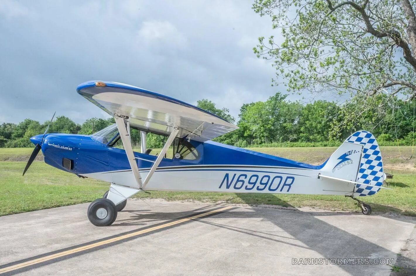 A blue and white single-engine taildragger aircraft (N6990R) with a checkered tail is parked on a concrete pad.