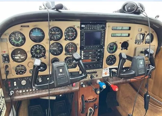 The cockpit instrument panel of the aircraft, featuring analog gauges, a modern GPS unit, and two control yokes.