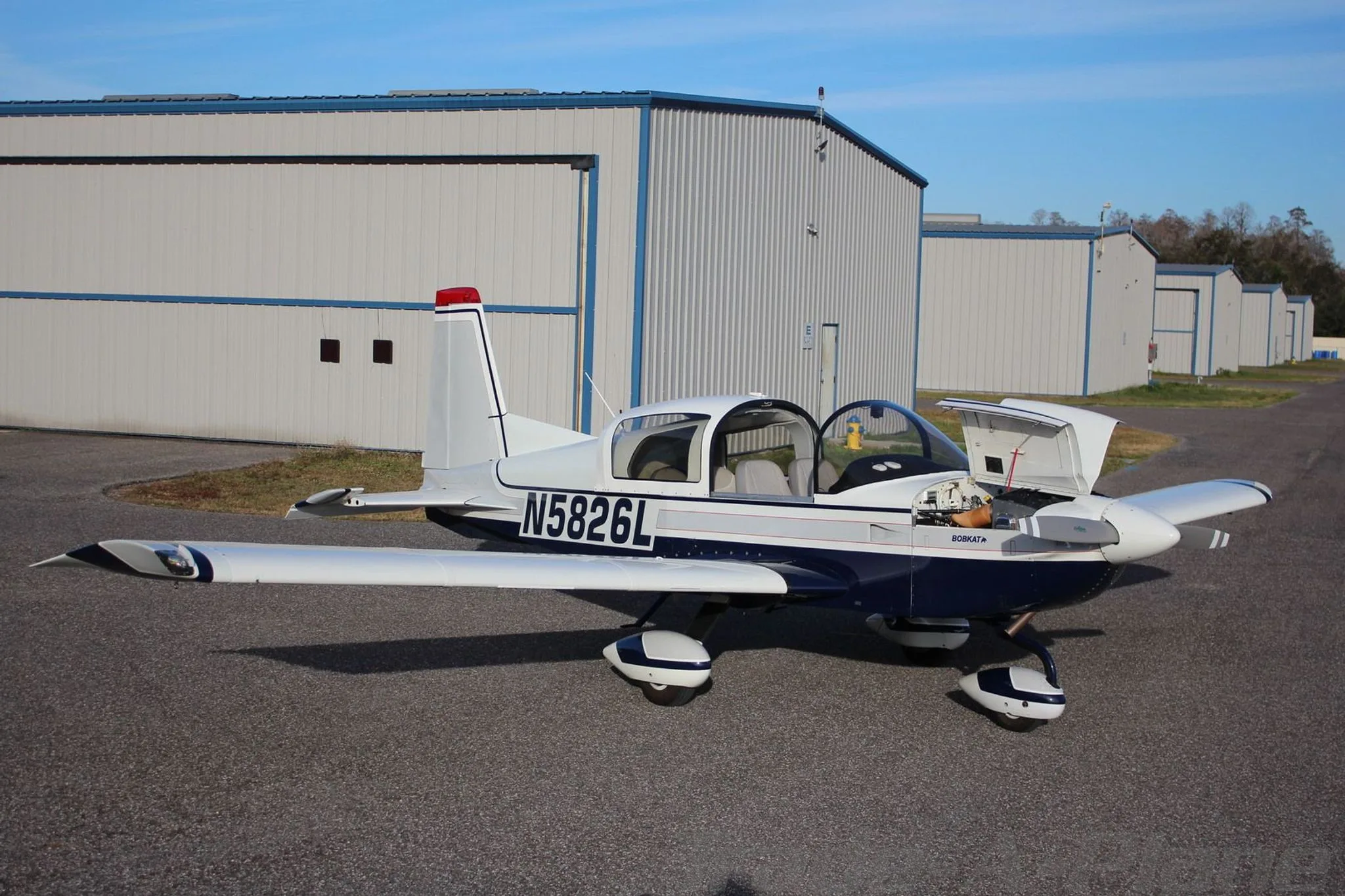 A white and blue Grumman AA-5B Tiger aircraft (N5826L) with its engine cowling open, parked on an airfield.