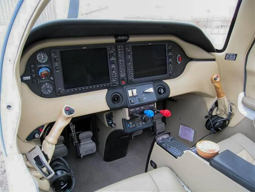 The cockpit of a small aircraft, featuring a tan dashboard with two large glass displays and traditional controls.