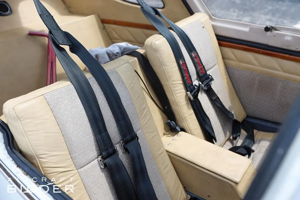 The tan and beige rear seats of the aircraft cabin with black seatbelts.