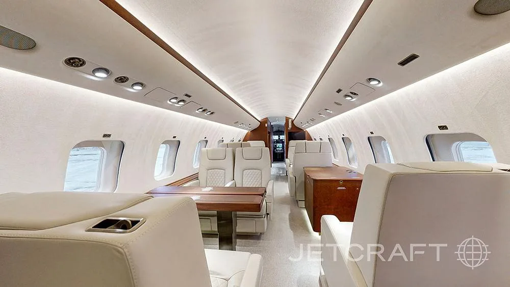 A view of the aircraft's interior cabin showing cream-colored seats and a wooden dining table.