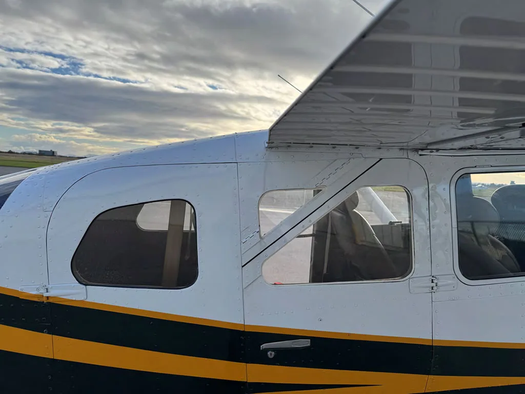 A close-up view of the cabin windows and upper fuselage of the dark green and white Cessna 182.