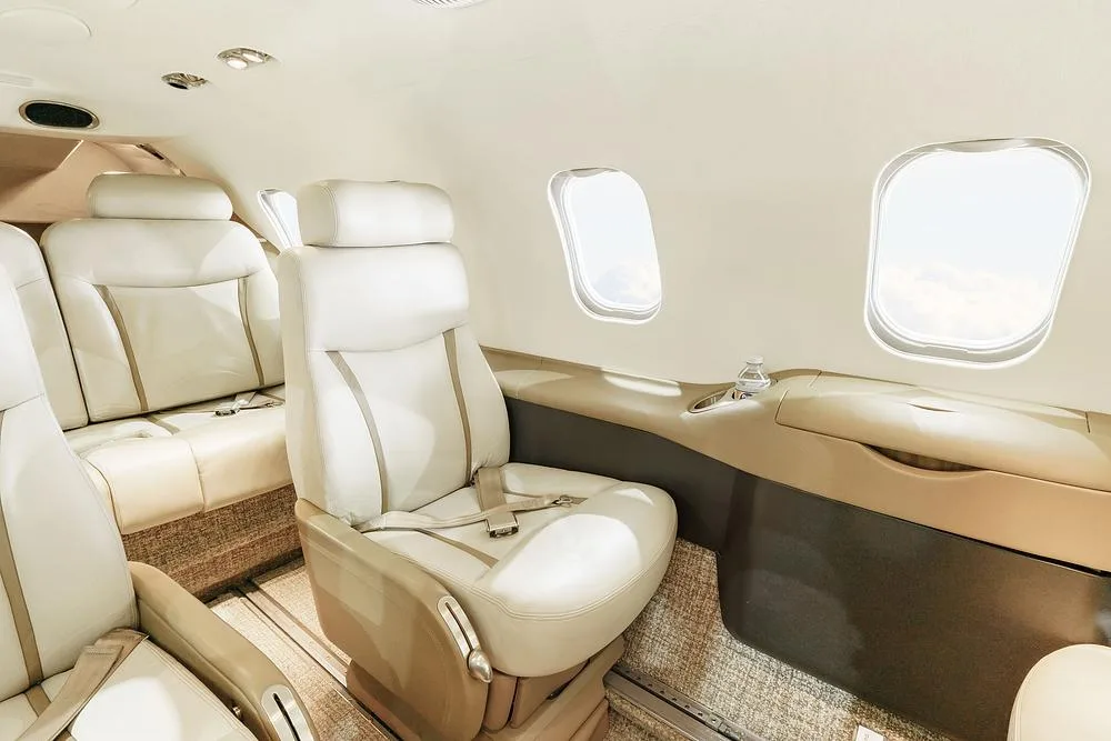 A close-up view of two light-colored leather passenger seats next to windows in an aircraft cabin.