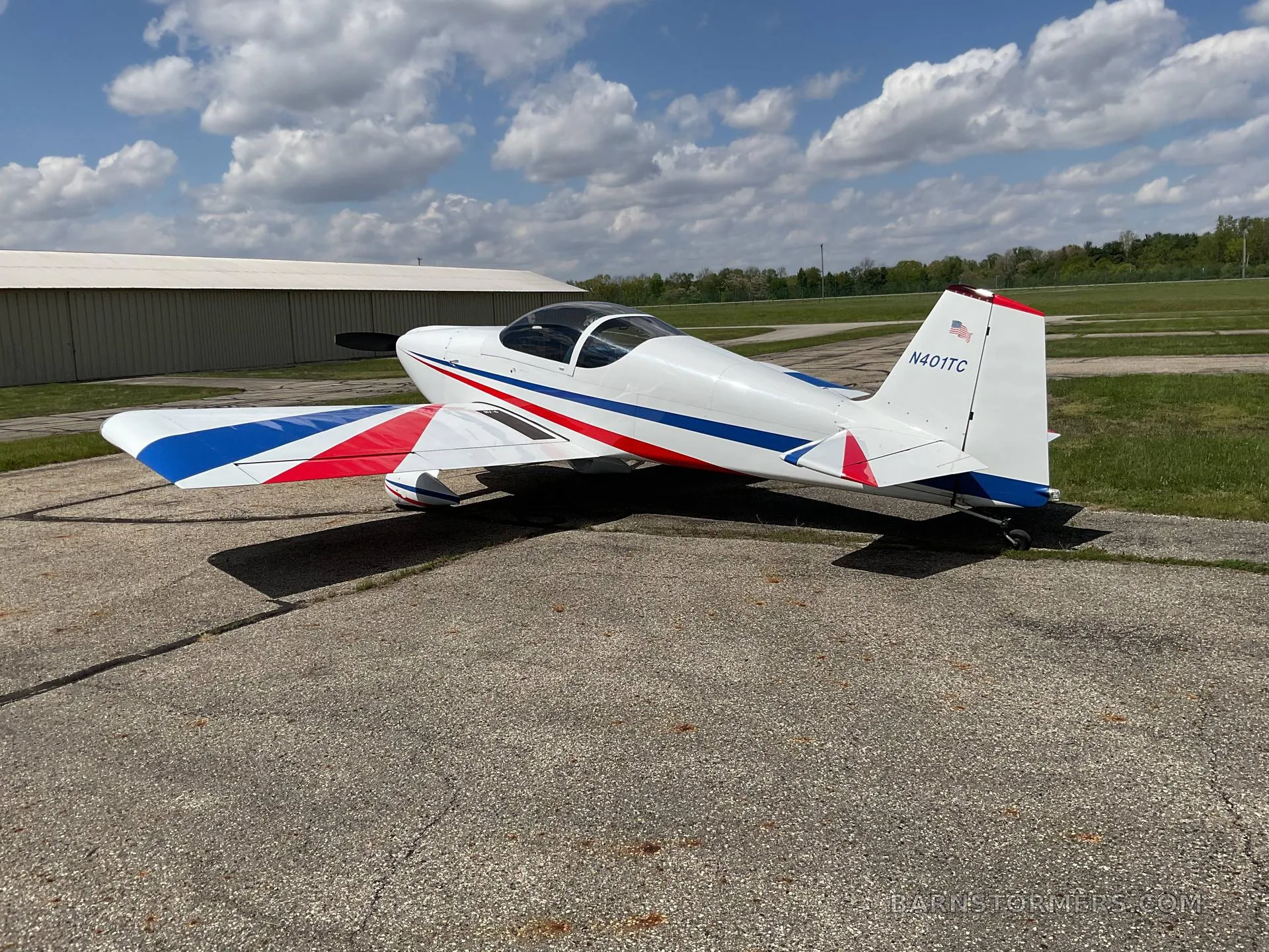 A white single-engine aircraft with red and blue stripes on its wings and tail (N401TC), parked on an asphalt tarmac under a partly cloudy sky.
