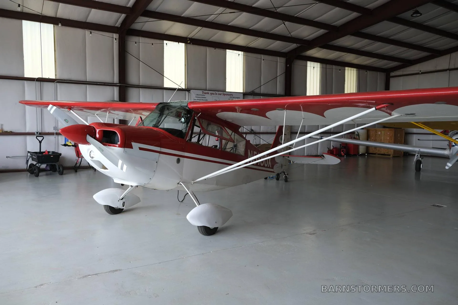 A red and white single-engine aircraft with high wings, parked inside a hangar.