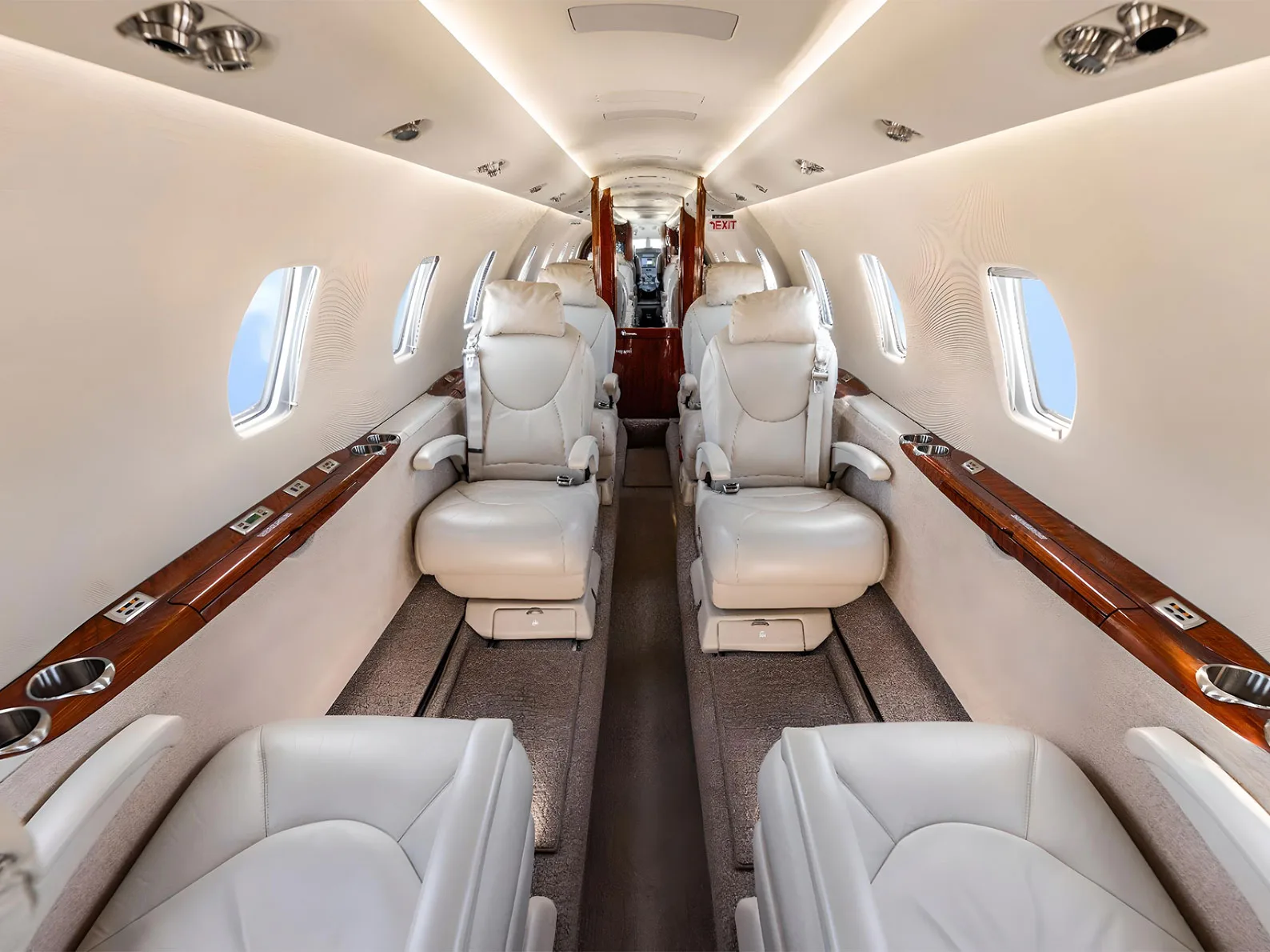 The luxurious cabin interior of a private jet with light-colored leather seats and wood accents.