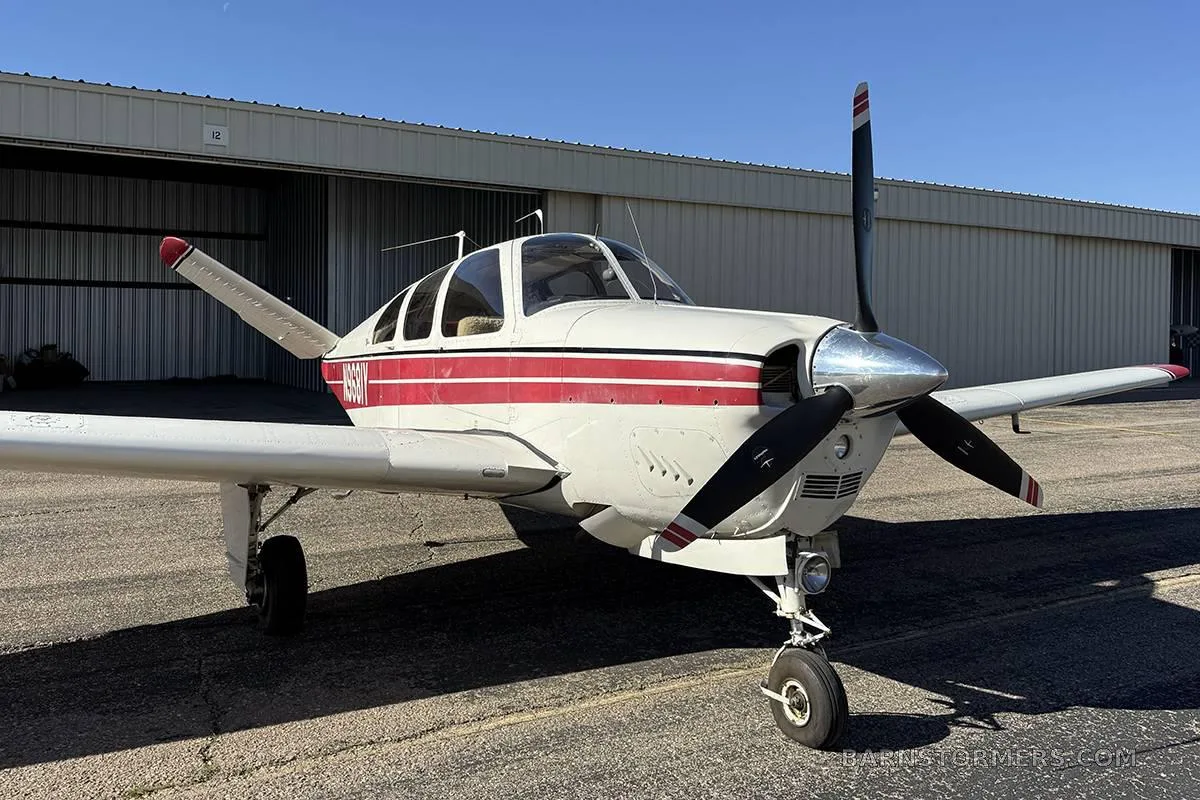 A white single-engine aircraft with red stripes and a black propeller parked on a tarmac in front of a hangar.