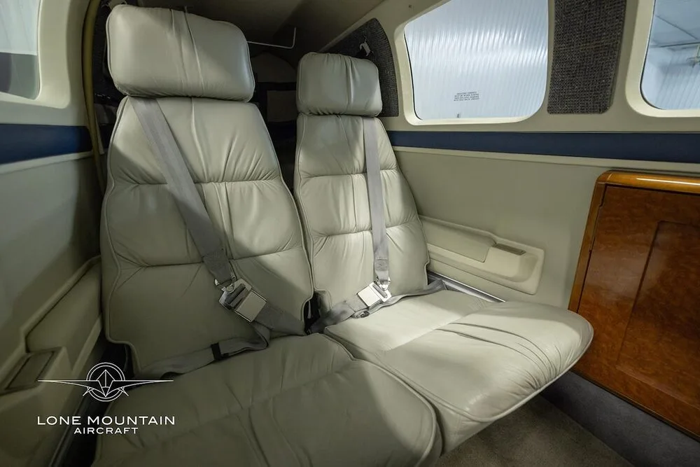 A close-up view of the light gray leather passenger seats and wood trim in the cabin of a Beechcraft Bonanza A36.