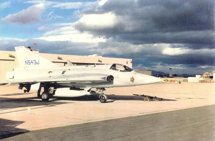 A white Saab Draken aircraft with registration N543J sits on an airfield tarmac under a cloudy sky.