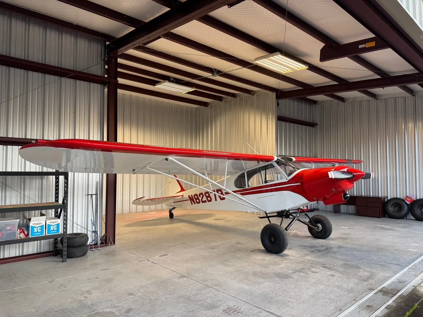 A red and white bush plane, N8287B, with large tires, parked inside a hangar.