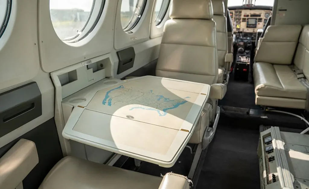 The interior cabin of a private aircraft, showing beige seats and a fold-out table with a map design.