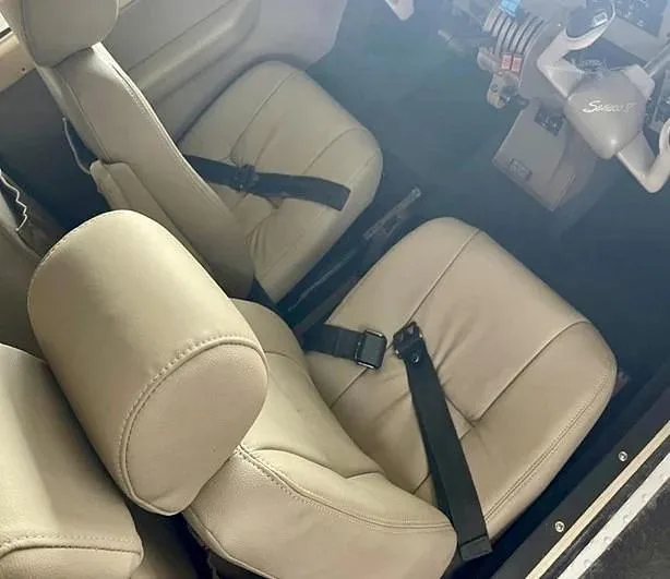 Light beige leather seats with seatbelts are visible in the aircraft's cabin, with cockpit controls in the background.