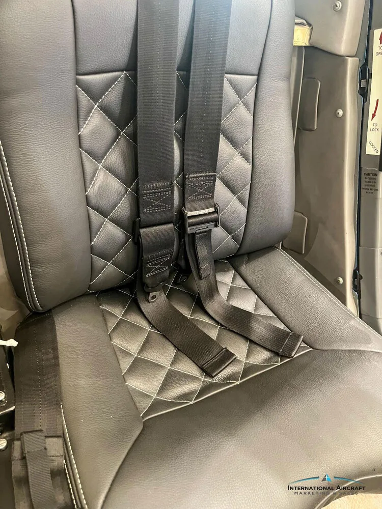 A close-up of a black leather helicopter seat with white diamond stitching and a black four-point harness.