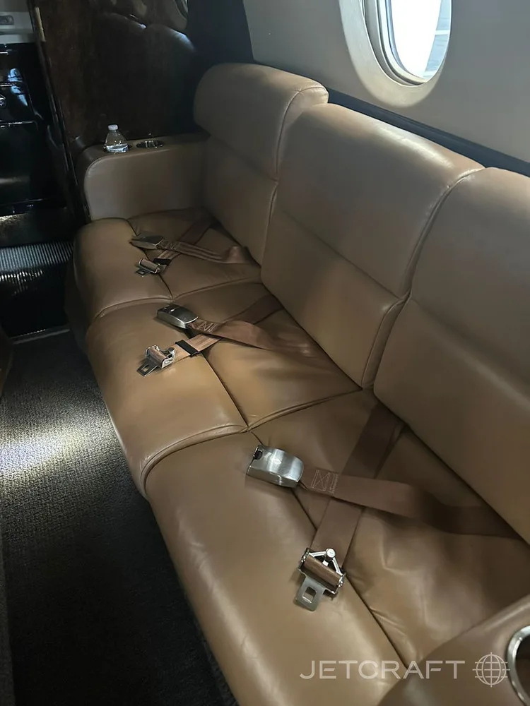A three-person tan leather bench seat with seatbelts in a private jet cabin.