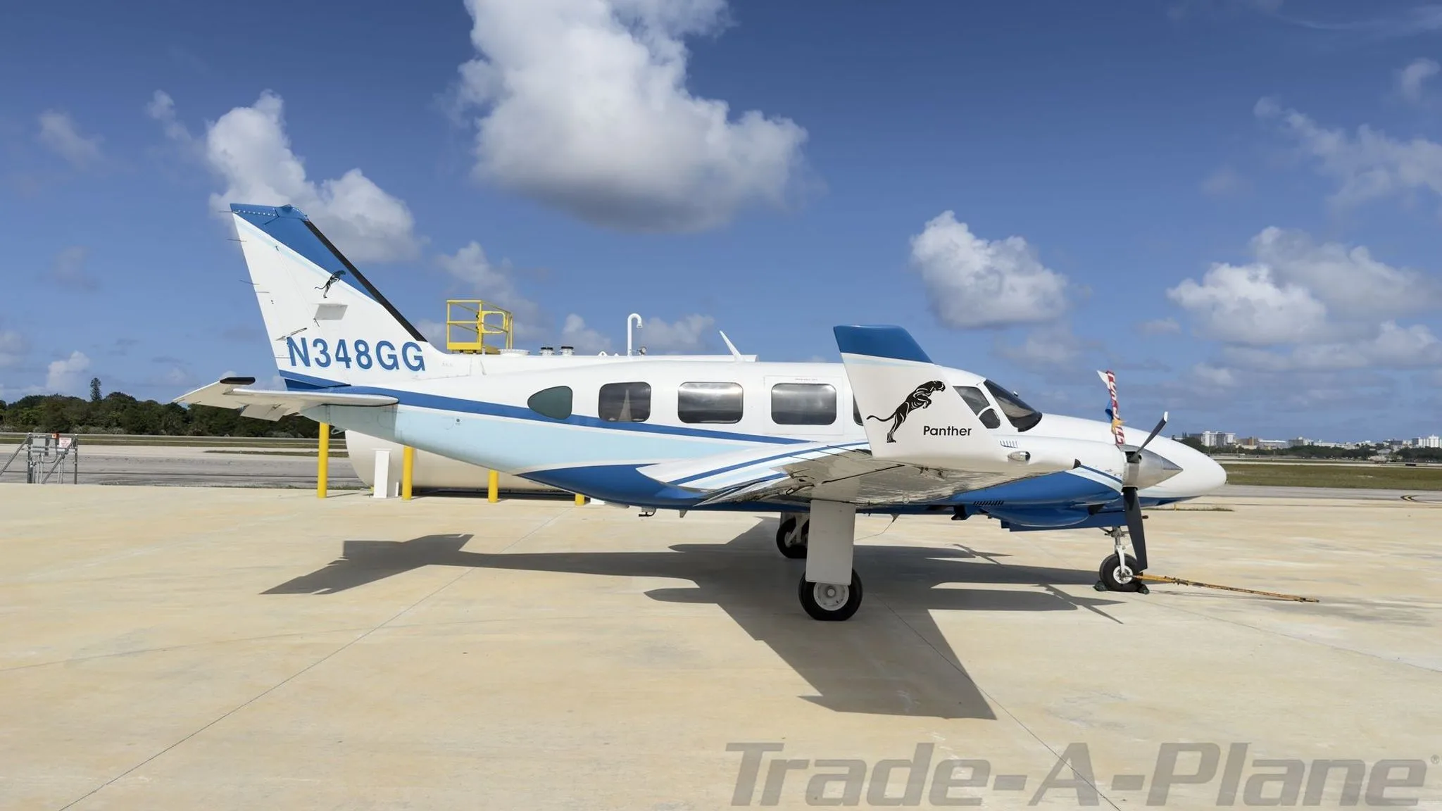 Side view of a white and blue twin-engine propeller aircraft, N348GG, featuring a 'Panther' decal on the fuselage, parked on a concrete ramp.