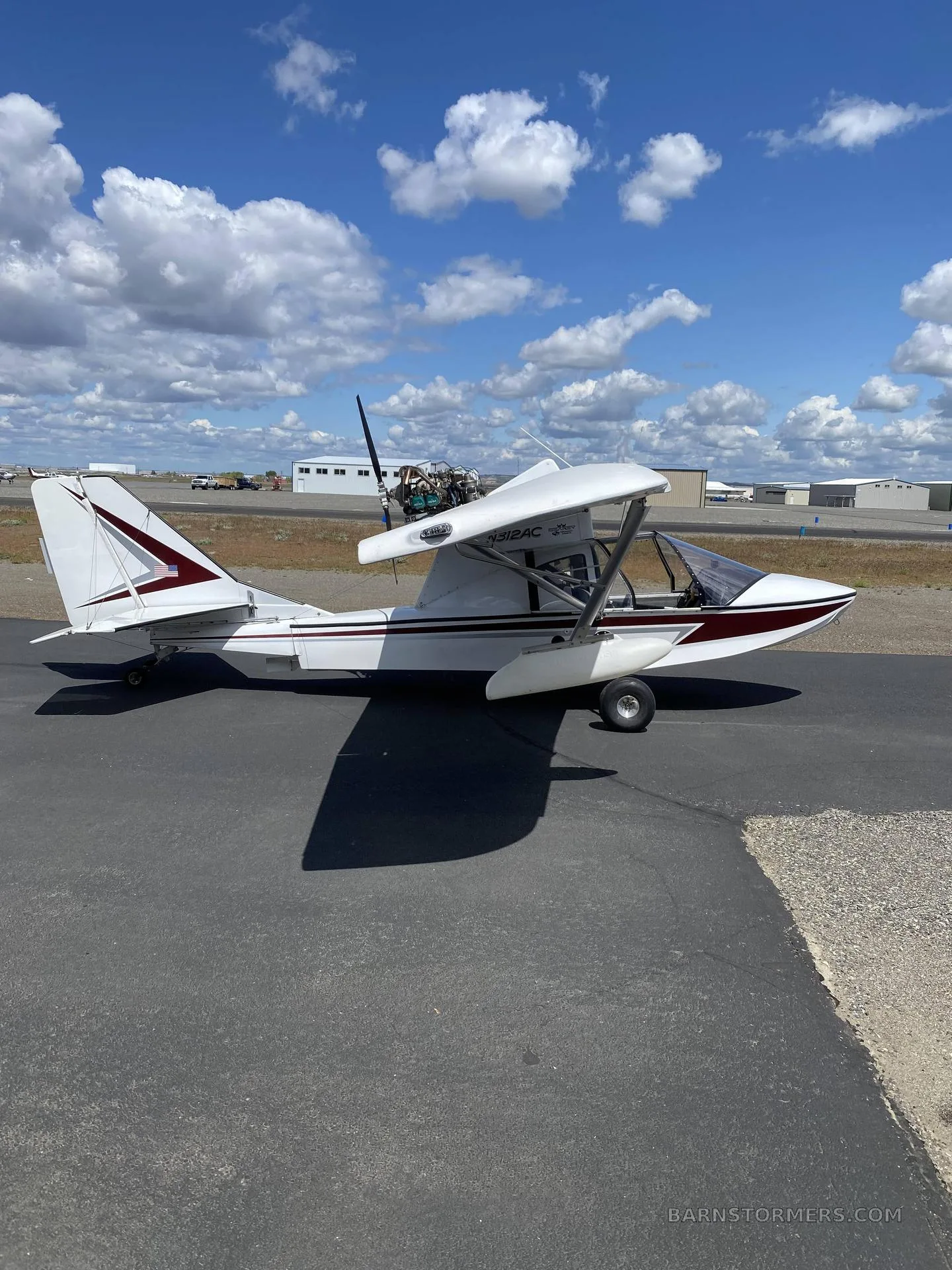 A white and maroon Searey amphibian aircraft with registration N312AC is parked on an asphalt ramp under a partly cloudy sky.