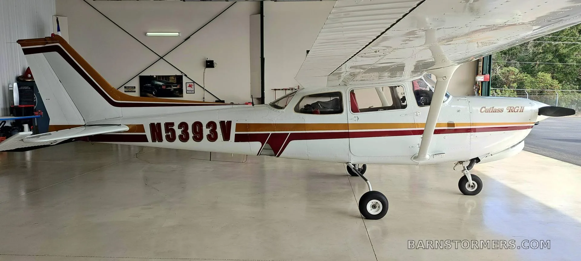 A white Cessna Cutlass RGII (N5393V) with red and gold stripes is viewed from the right side inside a hangar.
