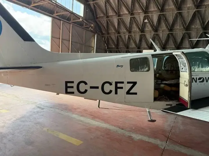 Side view of a white twin-engine propeller aircraft with registration EC-CFZ and an open door inside a hangar.