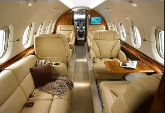The luxurious cabin interior of a business jet with beige leather seating, a sofa, and wood accents.