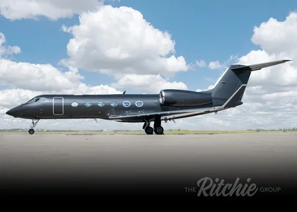 A dark grey Gulfstream G550 business jet is parked on an airfield under a partly cloudy sky.