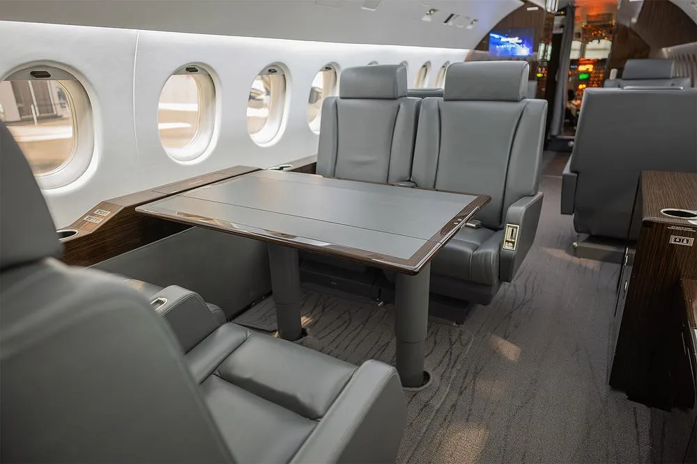 A section of the business jet's cabin interior with grey leather seats and a deployable table.