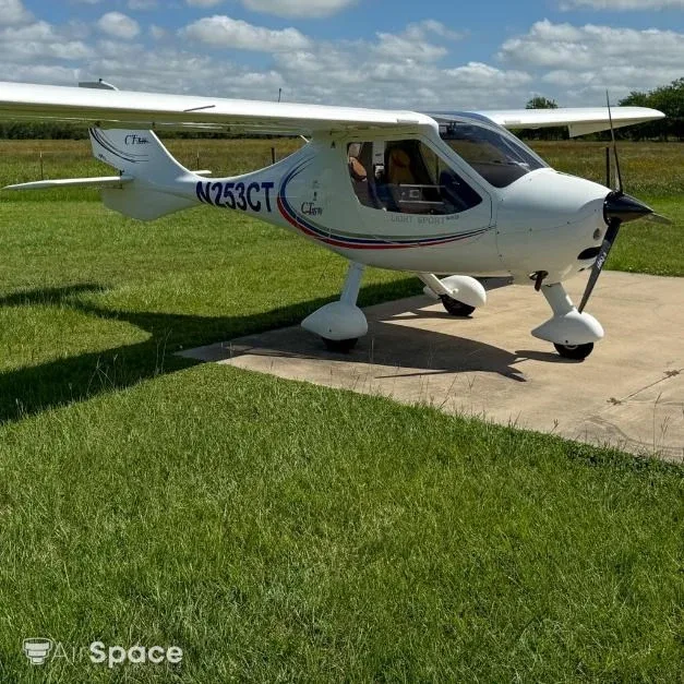 A white Flight Design CT Light Sport aircraft, N253CT, is parked on a concrete pad next to grass under a partly cloudy sky.