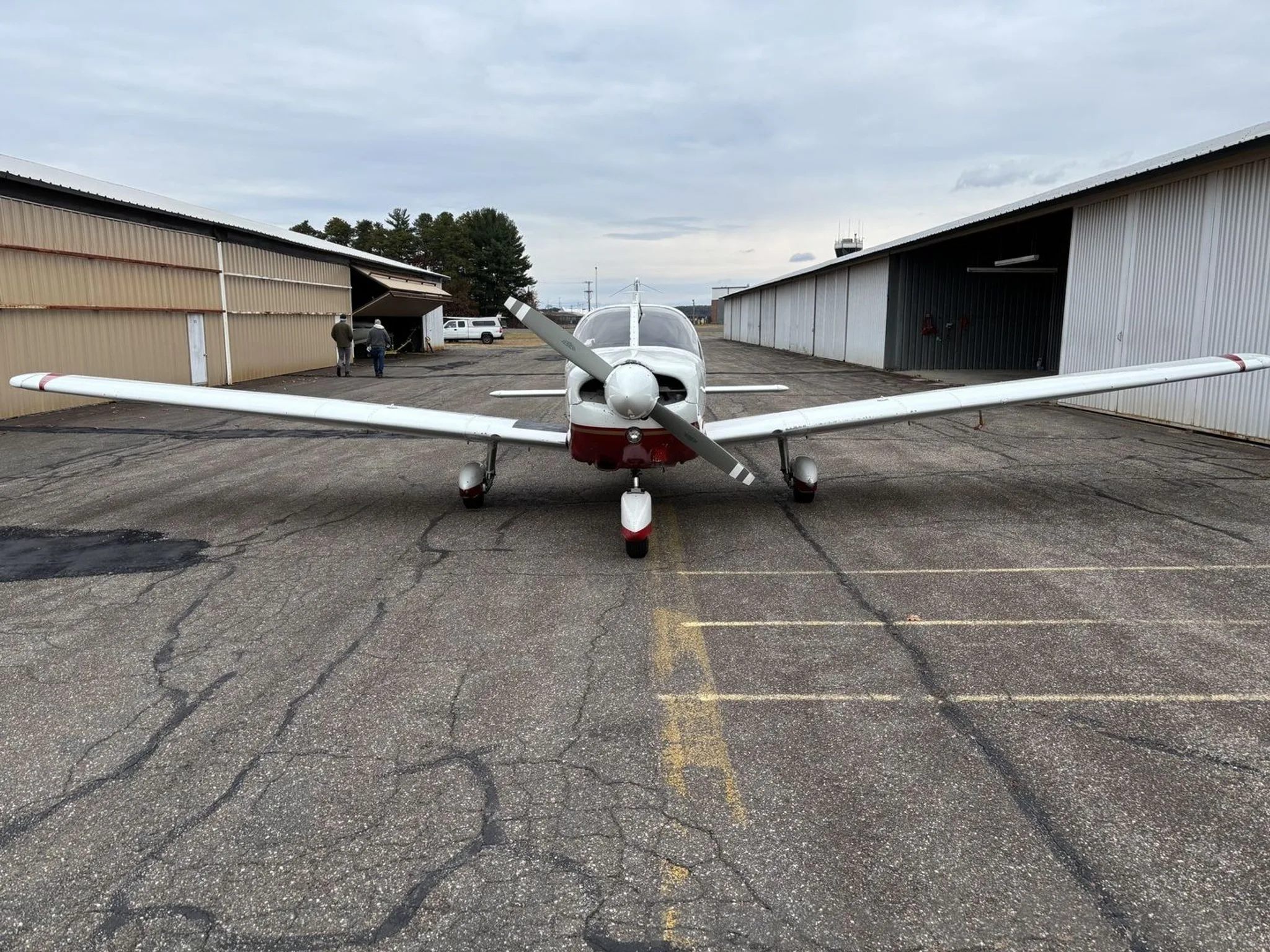 A front view of a white and red Piper aircraft, N8578C, parked on an asphalt ramp between hangars.