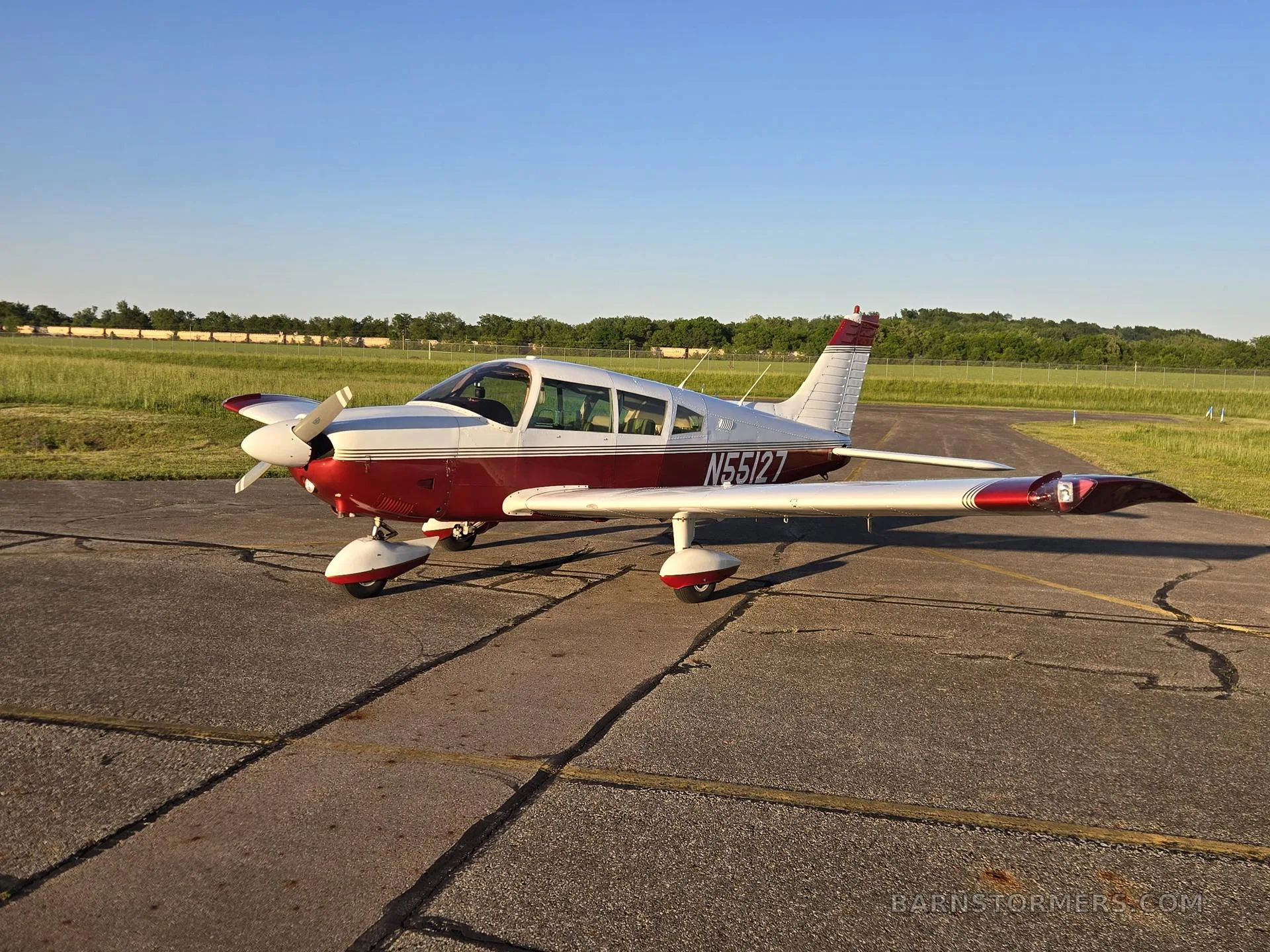 A red and white single-engine propeller aircraft with registration N55127 is parked on an asphalt ramp under a clear blue sky.
