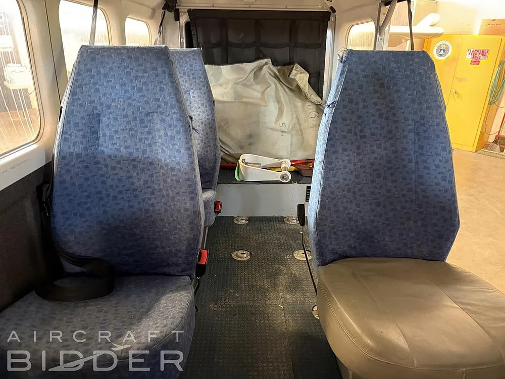 The interior cabin of the aircraft, showing blue fabric seats and a grey floor, with some cargo in the rear.