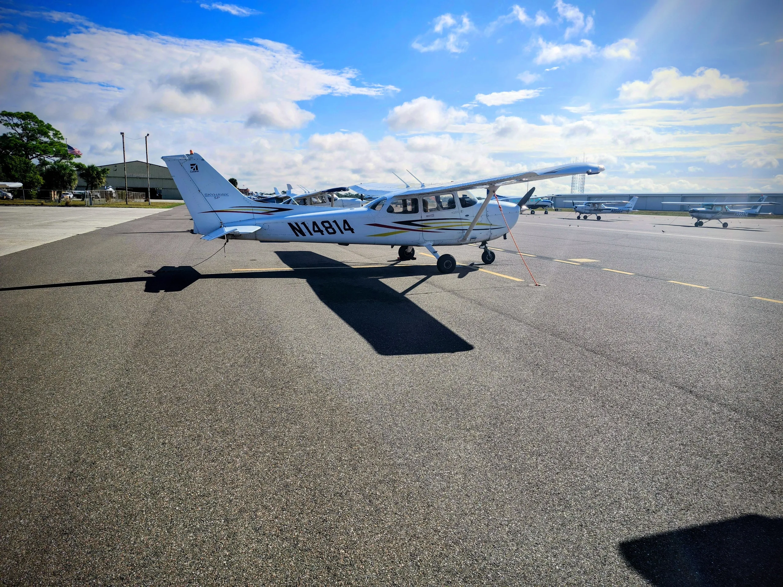 A white Cessna N14814 aircraft is parked on an airport tarmac under a bright blue sky with clouds.