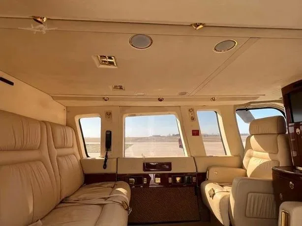 The helicopter's cabin shows a cream-colored bench seat and individual chairs with large windows.