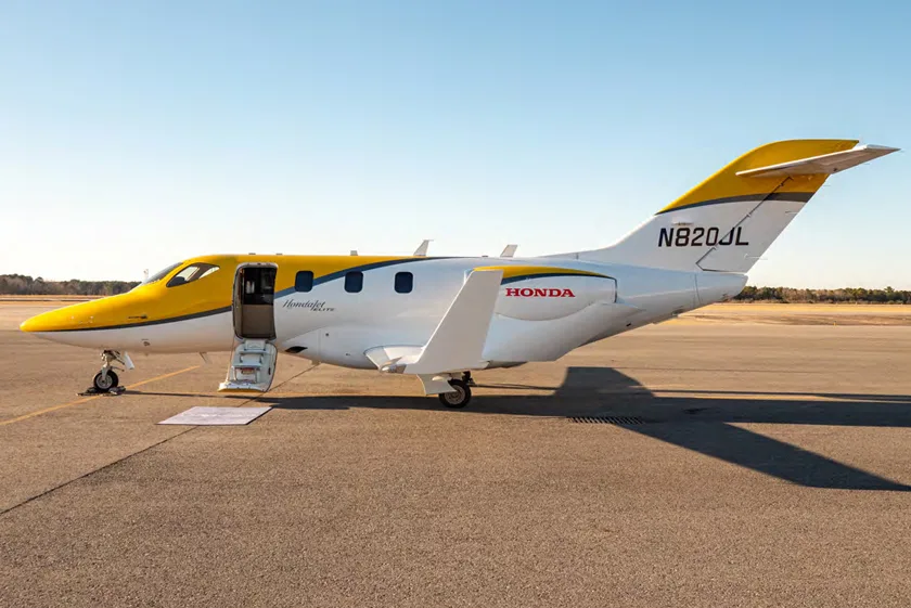 HondaJet with yellow and white paint scheme parked on the tarmac with the door open.