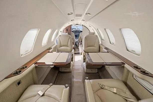 The luxurious cabin interior of a Cessna Citation CJ3 with beige leather seats and fold-out tables.