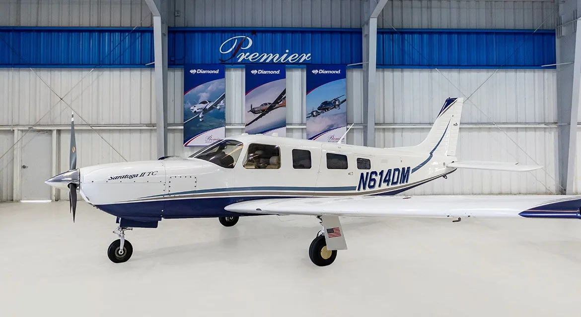 A white and blue Piper Saratoga II TC aircraft, registration N614DM, parked in a hangar.