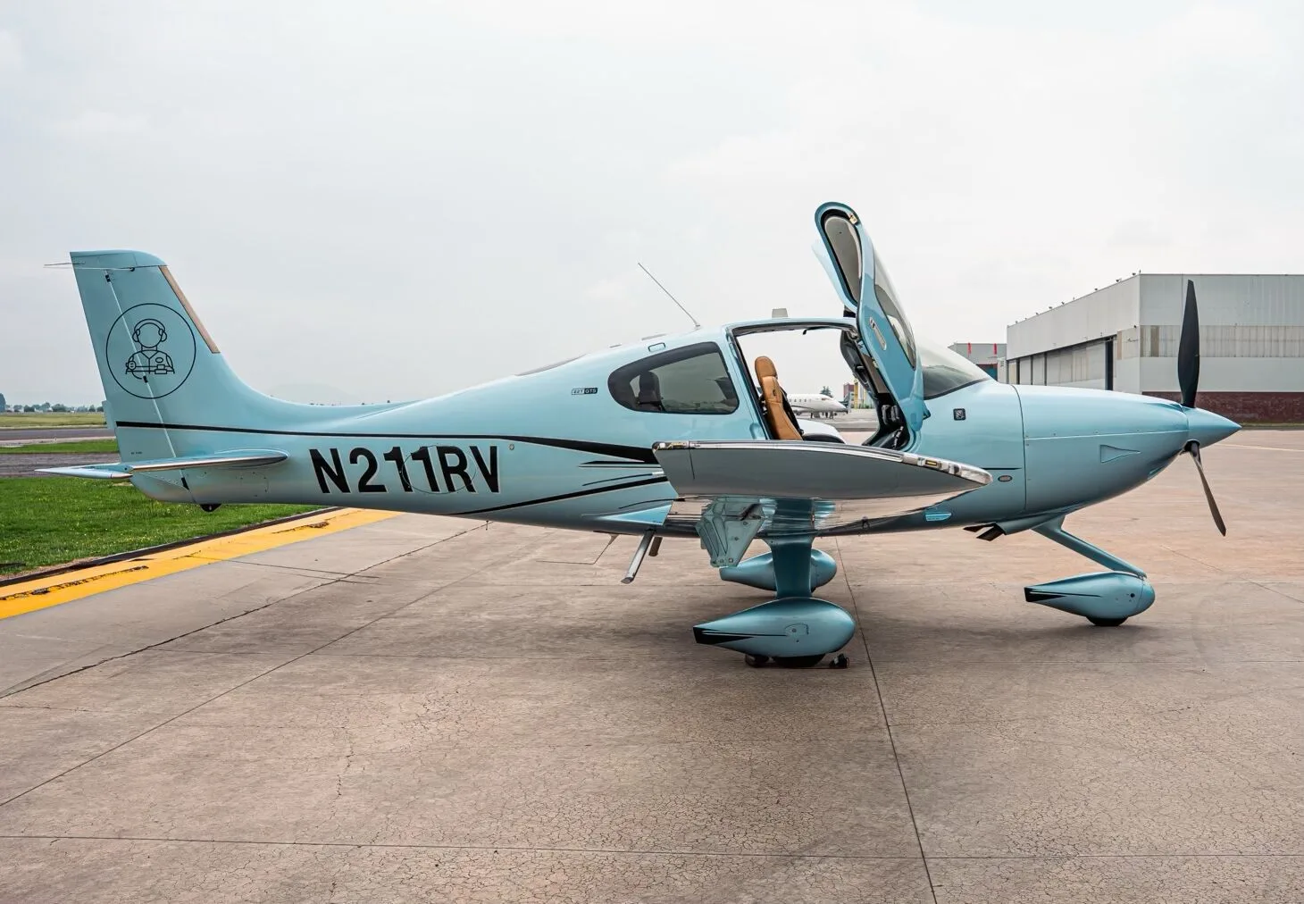 A light blue Cirrus SR22T aircraft with registration N211RV parked on an airfield, showing the left side with the door open.