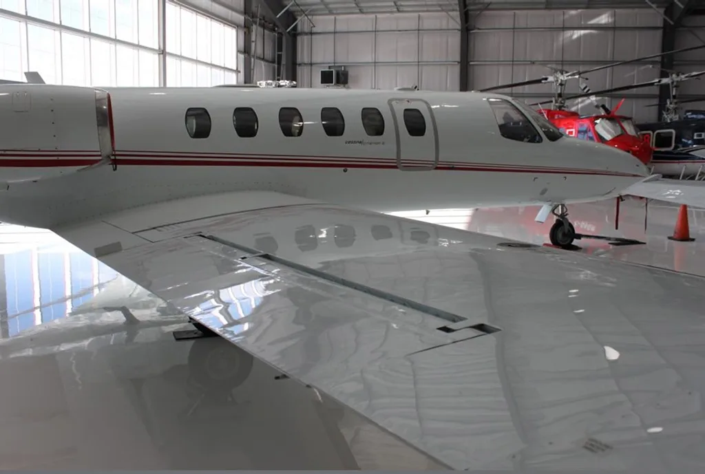 A close-up view of the right wing and fuselage of a white Cessna Citation aircraft in a hangar.