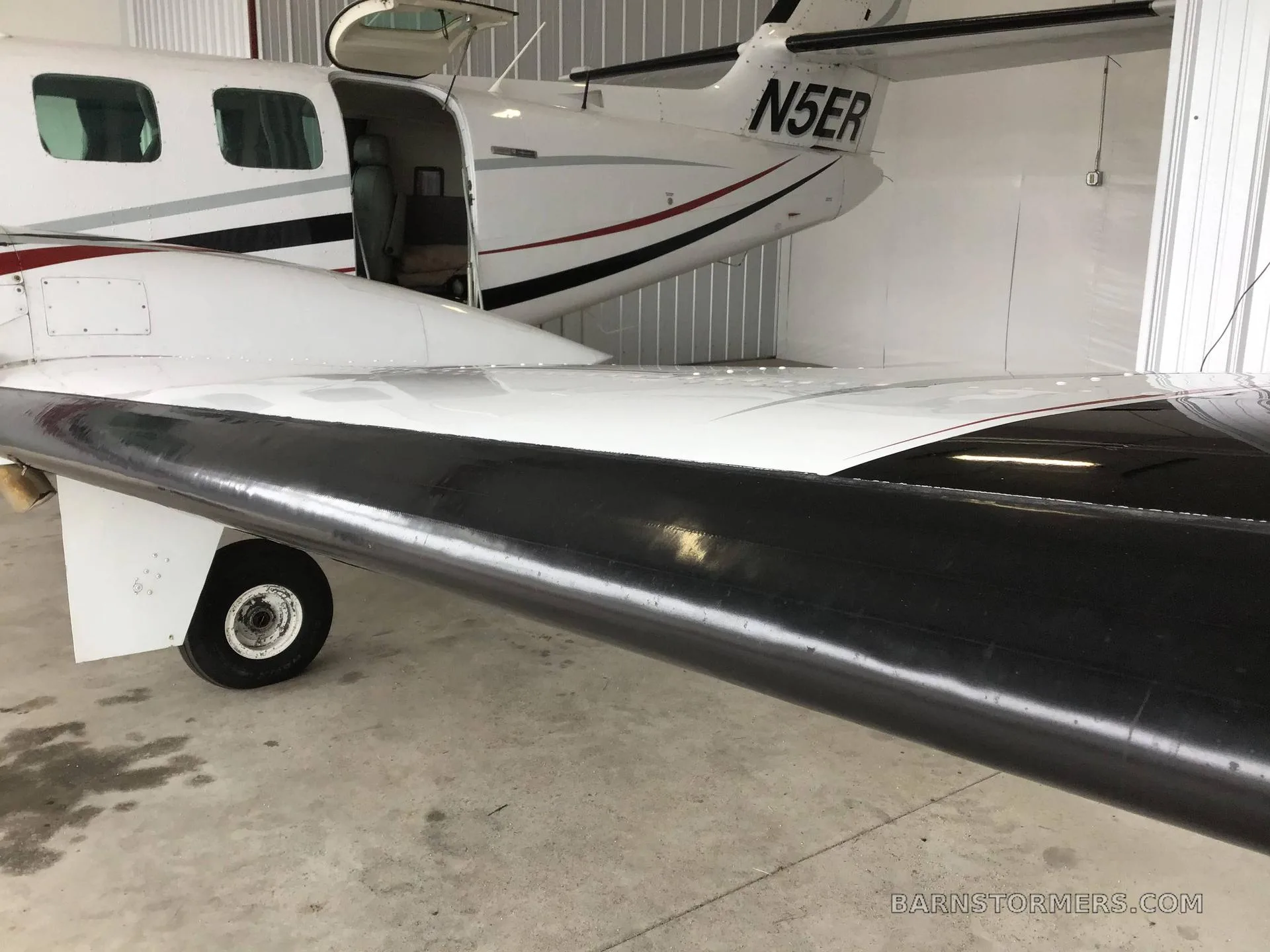 A close-up view of the rear fuselage, tail, and black wing of a white twin-engine aircraft with registration N5ER, parked in a hangar.