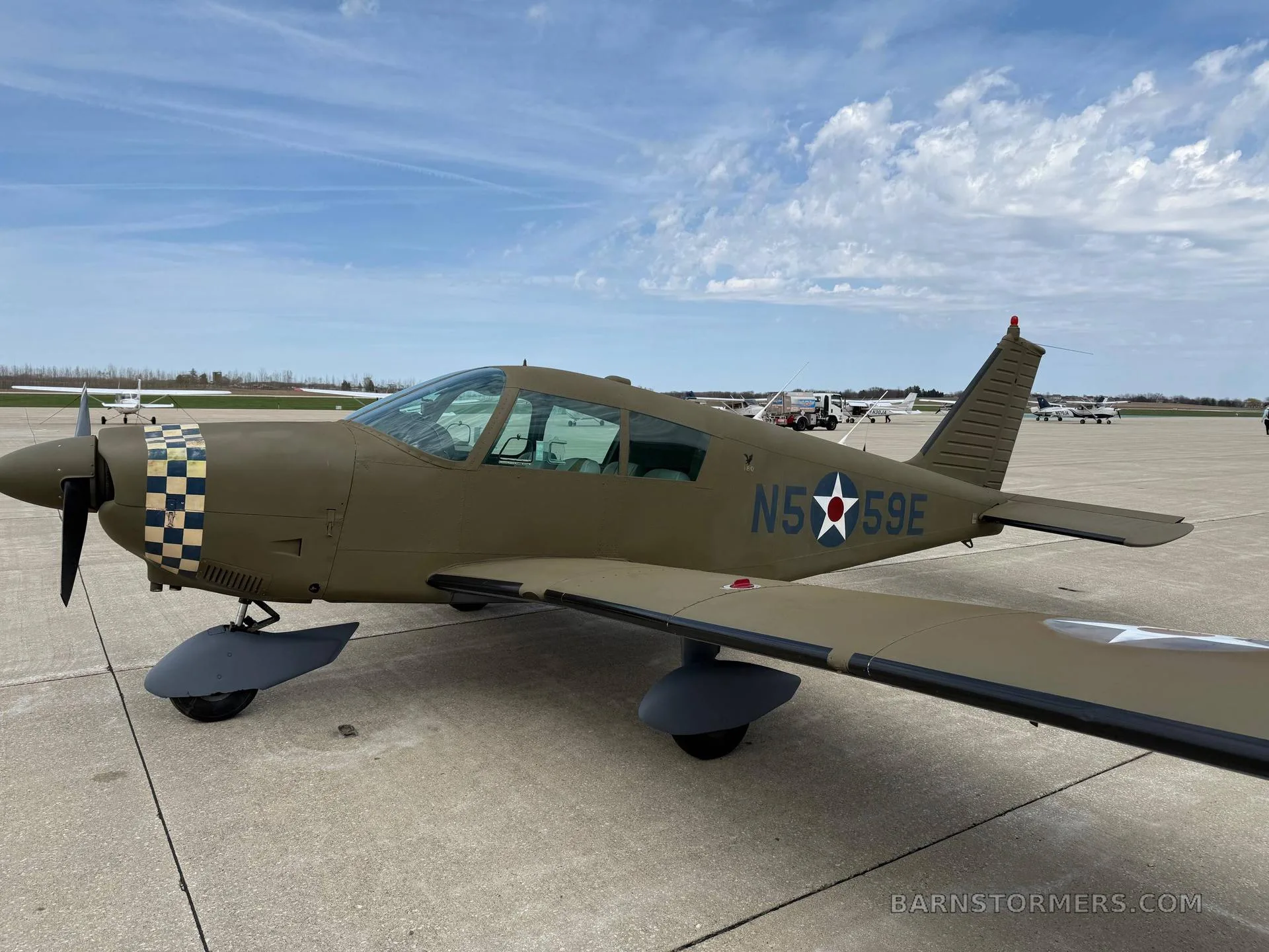 A green single-engine propeller aircraft with a checkered nose and US star insignia, parked on an airfield.
