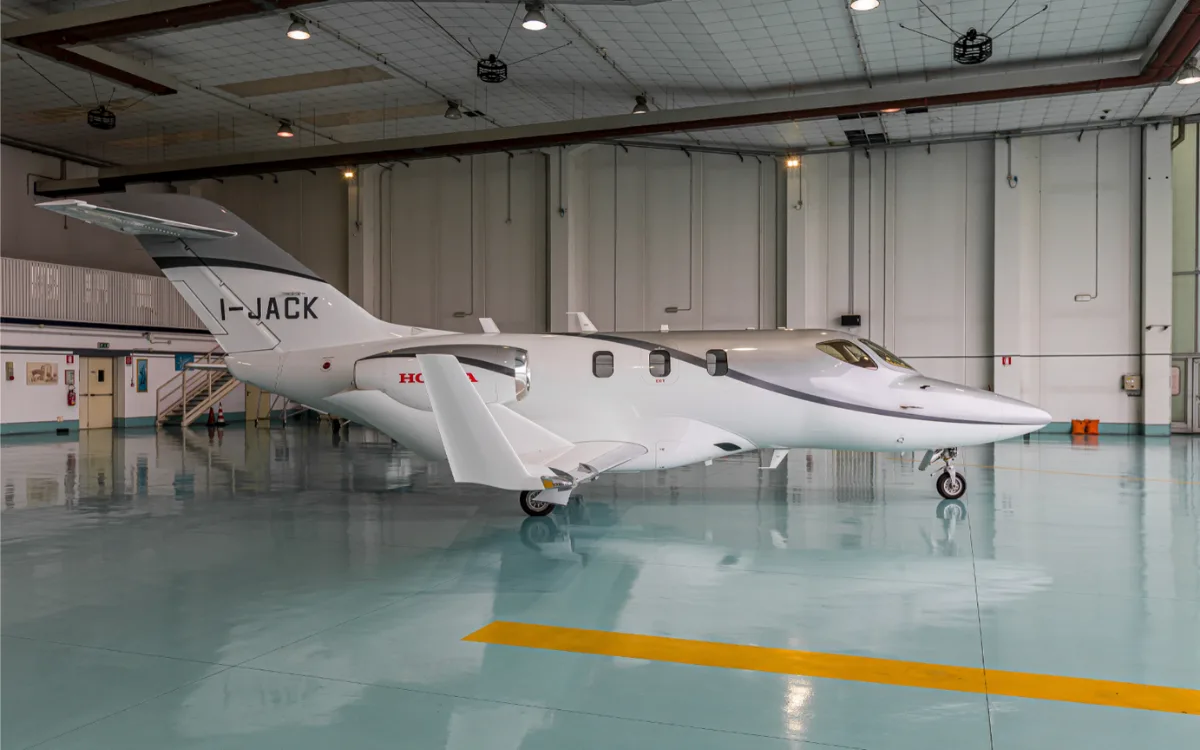 A white and silver HondaJet with registration I-JACK parked inside a hangar.