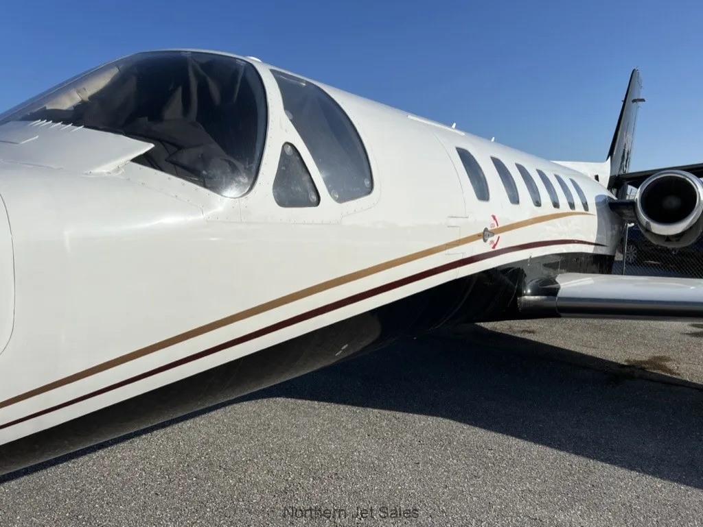 Close up of the fuselage of a white and black jet with gold accent stripes.