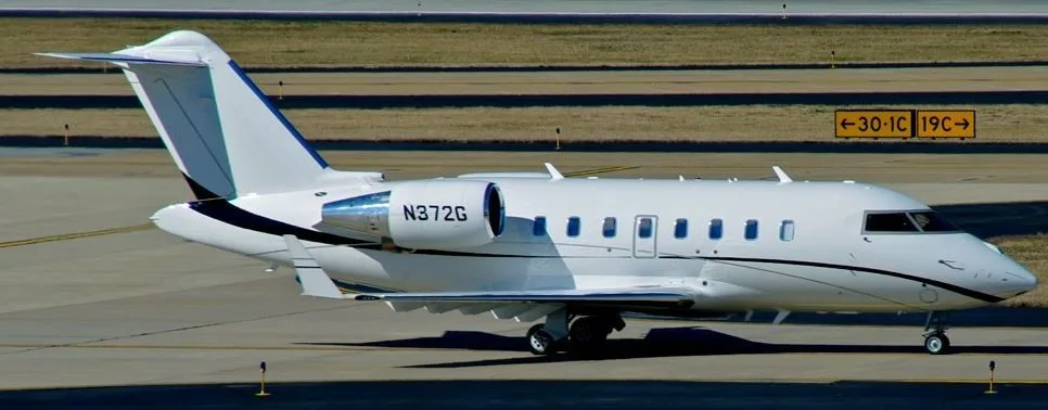 A white Bombardier Challenger 605 aircraft with registration N372G is seen on an airport tarmac.